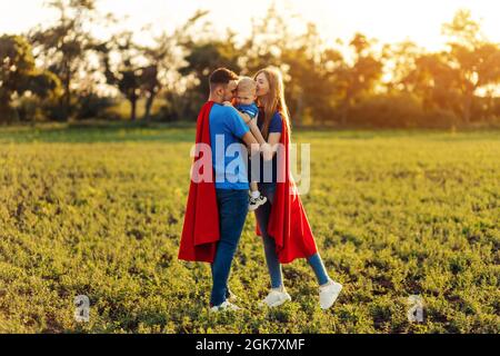 Konzept der europäischen Superfamilie, im Freien, liebevoller Vater hält am Hals, Superhelden Familie bei Sonnenuntergang in der Natur geführt, Familie umarmt Stockfoto