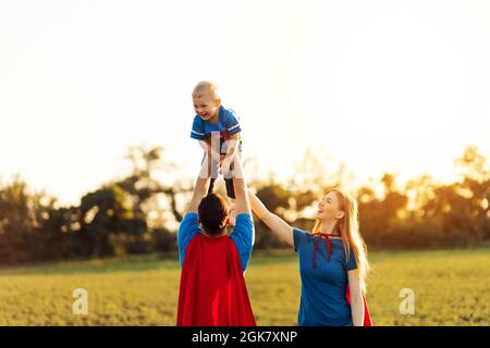 Konzept der europäischen Superfamilie, im Freien, liebevoller Vater hält am Hals, Superhelden Familie bei Sonnenuntergang in der Natur laufen, Vater hebt seinen Sohn in den Himmel Stockfoto