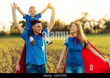 Konzept der europäischen Superfamilie, im Freien, liebevoller Vater hält am Hals, Superhelden Familie bei Sonnenuntergang in der Natur geführt, Vater trägt seinen Sohn auf seinem sh Stockfoto