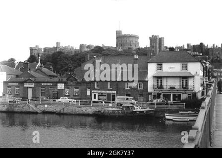 Die 1960er Jahre, historisch, von der Windsor Bridge aus gesehen, sehen wir einen Blick auf die Themse, eine Straße an der Themse in der historischen Stadt Windsor, in der englischen Hauptstadt von England. Die Stadt am Flussufer ist berühmt für ihr historisches Schloss, das in der Ferne auf der Skyline zu sehen ist und seit über 1,000 Jahren eine Residenz der britischen Königsfamilie ist. Salters Steamers, die Büros zu sehen sind, wurden 1858 gegründet und führten Vergnügungsfahrten auf und ab dem Fluss durch. Stockfoto