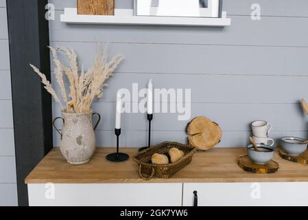 Wohnküche, Kerzen, Keramikvase mit getrockneten Blumen, Brötchen in einem Korbkorb, modernes Interieur Stockfoto