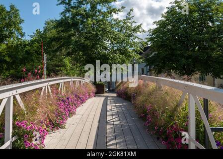 Hölzerne Fußgänger- und Fahrradbrücke über den Fluss Enkoping wunderschön dekoriert mit blühenden Petunia-Blumen, Bild aus Enkoping Schweden. Stockfoto