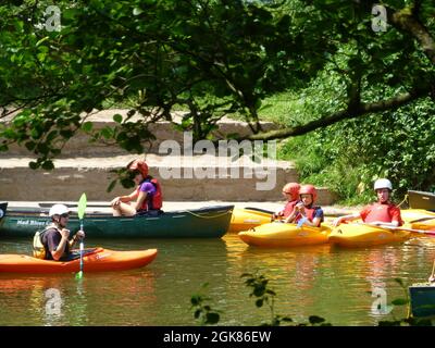 Menschen auf Booten im Forest of Dean Gloucestershire, Großbritannien, Kanus, Kanufahren, Kinder, die am Ufer des Flusses spielen, überqueren Helme, Helm, Paddel Stockfoto