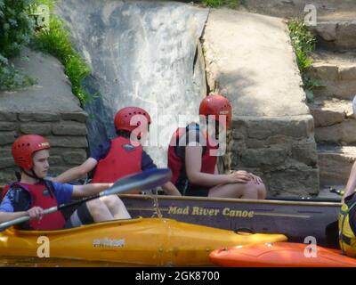 Menschen auf Booten im Forest of Dean Gloucestershire, Großbritannien, Kinder auf Kanus oder Kanus im River Wye mit roten Helmen an Felsen und Schwimmweste Stockfoto
