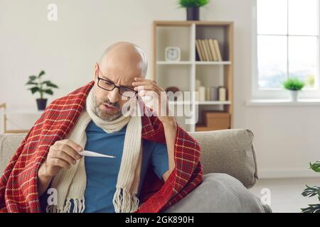 Kranker Mann mit Erkältung oder Grippefieber nimmt seine Temperatur und schaut auf das Thermometer Stockfoto