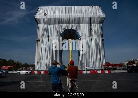 Paris, Frankreich. September 2021. Die Besucher fotografieren den eingewickelten Arc de Triomph, während die Arbeiter damit beschäftigt sind, den Wrapper, der an der Triomphe hängt, zu arrangieren. Der Triumphbogen wurde am 12. September gewickelt, um dem verstorbenen Künstler Christo zu Tribut zu zollen, der den Bogen vor seinem Tod in eine Packung wickeln wollte. Arbeiter wickelten es in einen recycelbaren und blauen Kunststoff und Band es mit einem roten Seil, wie Christo in seinem Projekt erwähnte. (Bild: © Abhijeet Gurjar/ZUMA Press Wire) Stockfoto