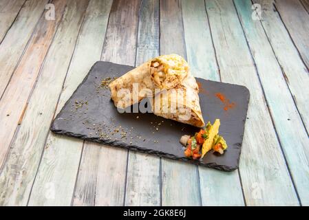 Beliebte mexikanische Weizen Tortilla Burrito Snack gefüllt mit Bohneneintopf und Huhn und weißem Reis mit Gemüse auf schwarzem Schieferteller Stockfoto