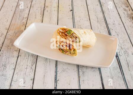 Gebratener panierter Hähnchen-Burrito mit einer Sauce aus Burrito mit Salat und Weizentortilla auf weißem Porzellanteller Stockfoto