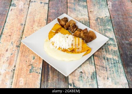 Venezolanischer Maiscachapa mit geschmolzenem Frischkäse und geriebenem Käse auf der Oberseite und Chicharon auf der Seite Stockfoto