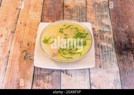 Glasschüssel mit peruanischem Rezept für gekochte Hühnerschühe mit gehacktem Gemüse auf einem quadratischen weißen Teller Stockfoto