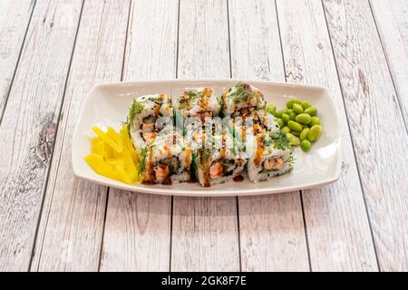 Uramaki california Roll gefüllt mit Lachs mit Teriyaki-Sauce, geriebenen Paprika und Edamame-Bohnen, frischem Dill und Nori-Algen auf weißem Tablett Stockfoto