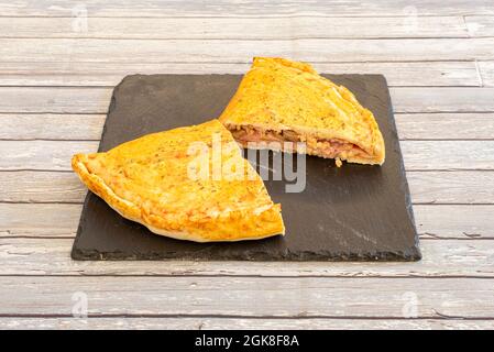 Teller mit italienischer gefüllter Calzone mit Schinken, Pilzen und Käse auf quadratischem Schieferteller Stockfoto