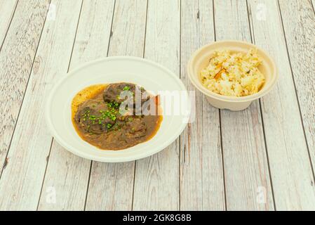 Spanische Schweinefleisch Wange Rezept mit weißem Reis garnieren in Haus Lieferbehälter auf weißem Holztisch Stockfoto