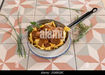 Iberische Wangen, die mit Pappardelle-Pasta in einer individuellen Pfanne auf einem Steinguttisch geschmort werden Stockfoto