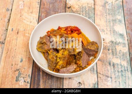 Tiefweißer Teller mit iberischen Wangen, geschmort mit einer Sauce aus Paprika und Karotten auf einem Holztisch Stockfoto