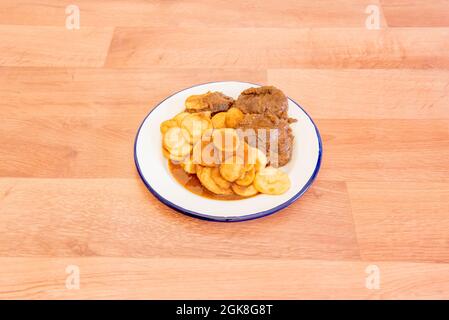 Fantastische Portion Schweinebacken in Sauce, garniert mit pommes frites und auf einem weißen emaillierten Teller Stockfoto