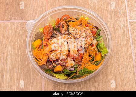 Gekochter Garnelensalat mit Rosenkohl, gebratenen Mandelscheiben, Kirschtomaten, Karotten, Mangostücken in einer Kunststoffschüssel zur Hauszustellung Stockfoto