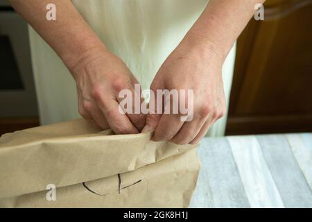 Weibliche Hände packen einen Papierbeutel mit dem gelieferten Essen aus. In der Zeit des Coronavirus ist die Methode der kontaktlosen Lebensmittelzustellung sehr beliebt. Stockfoto