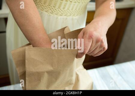 Weibliche Hände packen einen Papierbeutel mit dem gelieferten Essen aus. In der Zeit des Coronavirus ist die Methode der kontaktlosen Lebensmittelzustellung sehr beliebt. Stockfoto