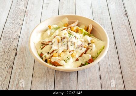 Cesar-Salat mit panierten Hähnchen und Mayonnaise, serviert in einer Schüssel mit Hauszustellung auf einem weißen Tisch Stockfoto