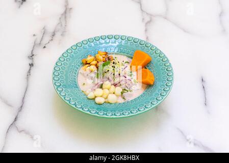 Klassische peruanische Ceviche mit mariniertem Seebarsch, Körnern aus zwei Sorten Mais, roter Zwiebel, Koriander, Süßkartoffel und einem schönen blauen Teller auf einem Stockfoto