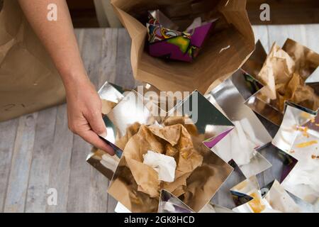 Weibliche Hände wickeln Papiertüten aus gelieferten Lebensmitteln. Altpapier wird zum Recycling in separaten Papierabfallbehältern abgelegt. Stockfoto