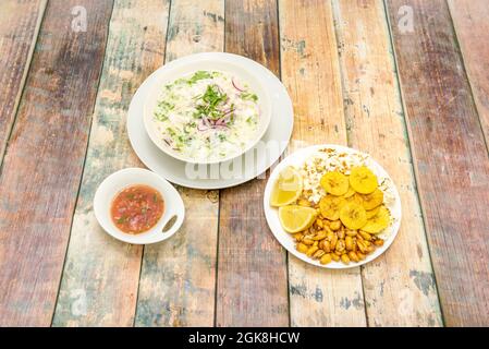 Weißer Fisch-Ceviche mit einer riesigen Hofgarnitur und einer Schüssel mit würziger Chilisauce auf einem Holztisch Stockfoto