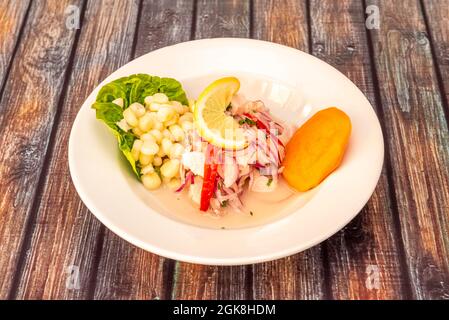 Fisch-Ceviche nach peruanischem Rezept mit Streifen von rotem Pfeffer, roter Zwiebel und süßer Kartoffelscheibe auf einem weißen tiefen Teller Stockfoto