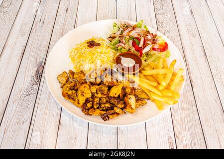 Hühnershawarma-Teller mit Pilau-Reis, Pommes Frites und türkischem Salat mit viel Zwiebel Stockfoto