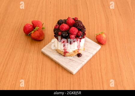 Individueller Käsekuchen mit allen Arten von roten Beeren und Marmelade auf einem grauen Marmorplatte und Holztisch Stockfoto