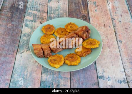 Typisches kolumbianisches Rezept für Chicharron, garniert mit gebratenen Kochbananen auf einem blauen Teller Stockfoto