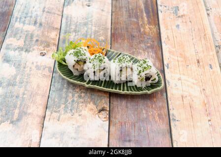 Vier Portionen Uramaki, gefüllt mit gebratenem Huhn und Nori-Algen mit gehacktem Schnittlauch auf einem grünen Tablett Stockfoto