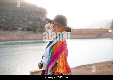 Frau mit schwarzem Hut in einem See und einer Fotokamera in der Hand, posiert und schaut auf die Kamera Stockfoto