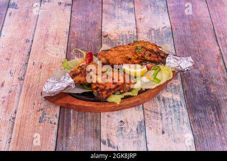 Hähnchenschenkel in Tandoori-Stil auf der Kochplatte mit Aluminiumfolie an den Rändern des Knochens auf dem Holztisch gegart Stockfoto