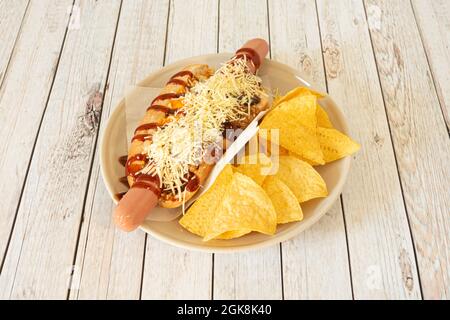 Würziger Hot Dog mit Chili, Grillsauce, geriebenem Käse und Maischips Stockfoto