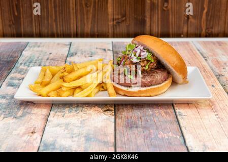 Rindfleisch-Burger mit mexikanischer scharfer Chili auf der Oberseite, Koriander und gehackte rote Zwiebel garniert mit Pommes frites Stockfoto