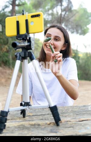 Fröhliche weibliche Teenager-Vlogger mit Jade Roller während der Aufnahme von Video auf Handy im Park Stockfoto