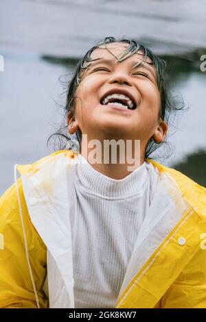 Content Asian Kind in Slicker suchen nach oben, während spielen an regnerischen Tag Stockfoto