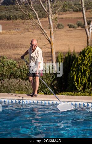 Ganzer Körper von älteren Männern in Brillen Reinigung Wasser im Schwimmbad mit Mopp im Hinterhof Stockfoto