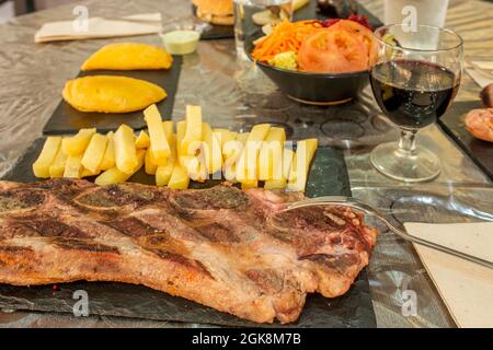 Gegrilltes Rippensteak in einem lateinischen Restaurant mit einem Glas Rotwein und Maisempanadas im Hintergrund Stockfoto