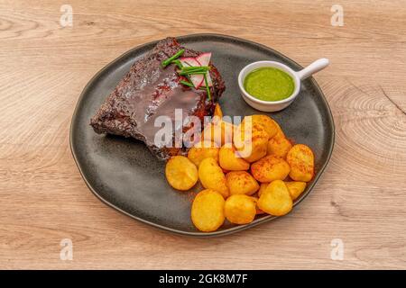 Rezept von Grillrippen mit gerösteten Kartoffeln zu Paprika mit grüner Mojo-Sauce auf einem schwarzen Teller Stockfoto