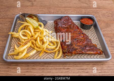 Marinierte Schweineribs, begleitet von lockigen Pommes Frites mit Limettendressing auf einem Metallblech Stockfoto