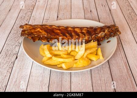 Gegrillte Rippchen im amerikanischen Stil mit Barbecue-Sauce und hausgemachten Pommes auf einem weißen Tablett Stockfoto