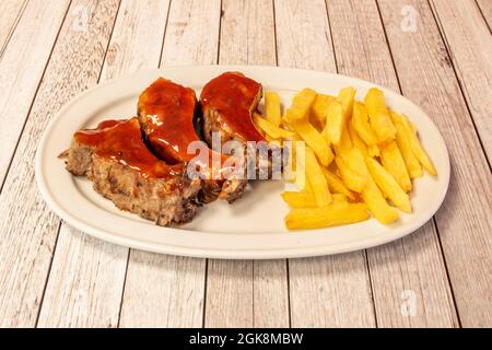 Ration von Rippchen, mariniert mit Barbecue-Sauce und hausgemachten Chips auf einem weißen Tablett auf dem Restauranttisch Stockfoto