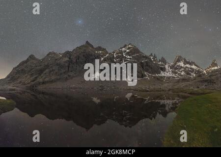 Malerische Landschaft von hohen felsigen Bergen mit Schnee bedeckt, die sich in ruhigem Wasser des Flusses unter sternenklaren Nachthimmel spiegeln Stockfoto