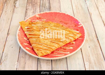 Salzige Crepe, gefüllt mit Hackfleisch mit Mayonnaise-Sauce und Ketchup auf einem roten Teller Stockfoto