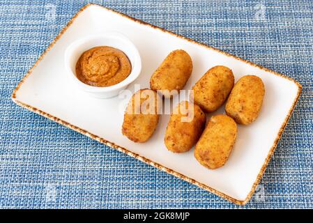 Portion Kroketten für spanische Tapa, begleitet von Sauce zum Eintauchen auf eine blaue Tischdecke Stockfoto