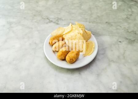 Kleine spanische Bar-Tapa mit Kroketten und Chips auf weißem Marmortisch Stockfoto