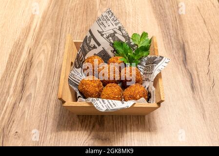 Tapa aus runden spanischen Kroketten mit Petersilie, serviert in einem Holzbehälter auf Holzboden Stockfoto