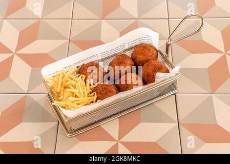 Ration von runden Kroketten mit Strohkartoffeln in individueller Fritteuse auf Steinzeugtisch Stockfoto